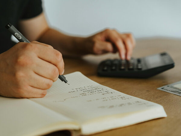 Person writing calculations in notebook using calculator